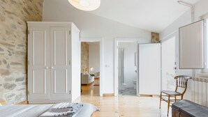 A spacious bedroom with a large bed, a wooden floor, a stone wall, and a wardrobe.