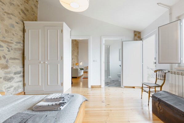 A spacious bedroom with a large bed, a wooden floor, a stone wall, and a wardrobe.