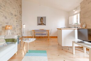 A modern living room with a sofa, a dining table, a TV, and a painting on the wall.