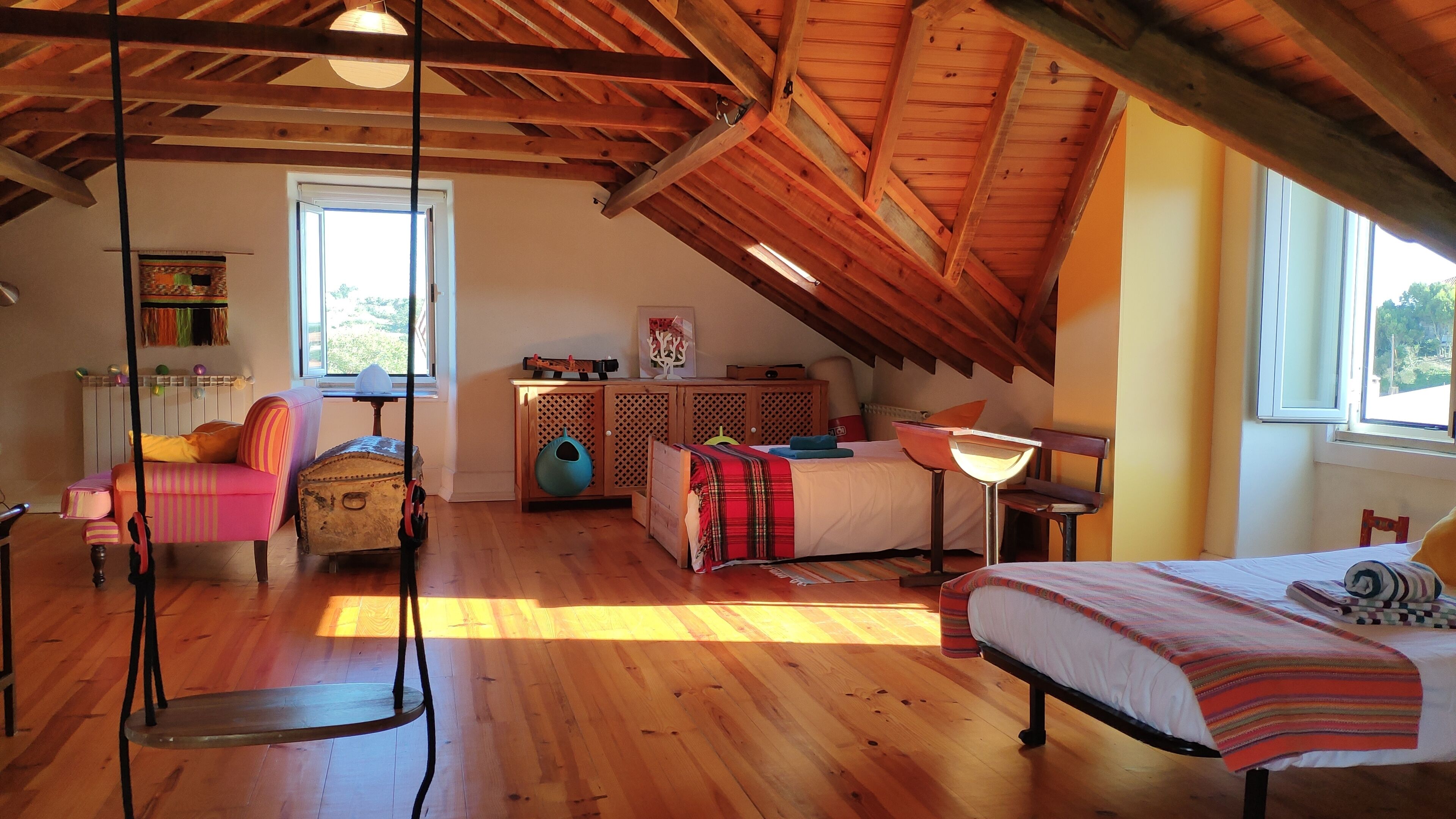 A cozy attic bedroom with a sloped ceiling, wooden beams, a bed, a desk, and a chair.