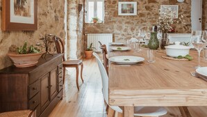 A rustic dining area with a wooden table set for a meal, surrounded by stone walls and wooden beams.