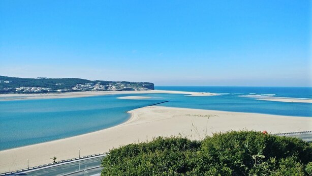 A coastal landscape with a sandy beach, calm waters, and a distant cliff.