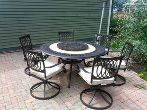 Une table ronde pour l’extérieur, accompagnée de quatre chaises, chacune dotée d’un siège et d’un dossier rembourrés, et agrémentée d’un élément décoratif central.