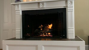 Une cheminée blanche avec un manteau de cheminée, un feu qui crépite à l’intérieur et un tapis sur le sol.
