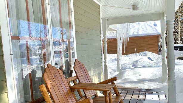 Une terrasse en bois avec deux fauteuils Adirondack et une véranda couverte.