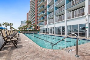 A swimming pool with lounge chairs and a building with balconies.