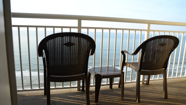 To flettede stole og et lille bord på en balkon med udsigt over havet.