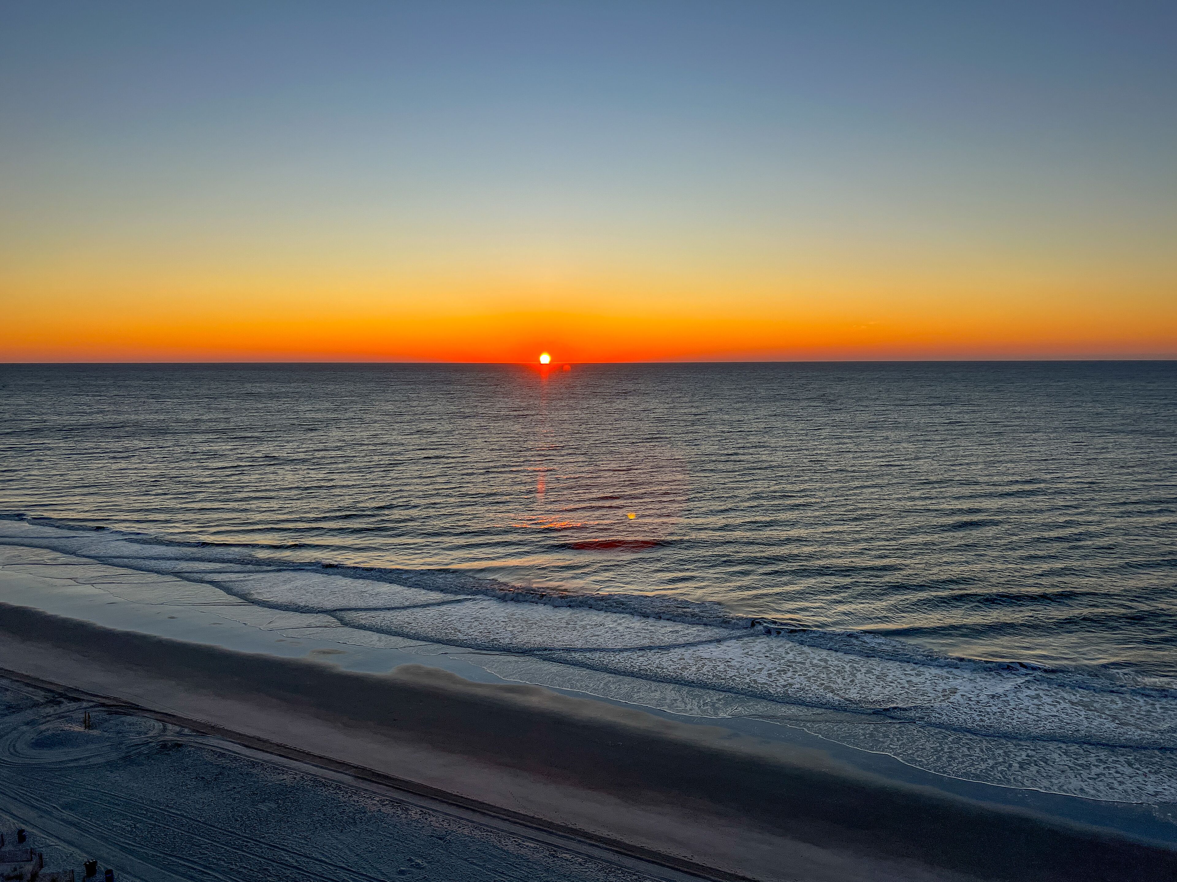 A beach at sunset with the sun setting over the horizon.