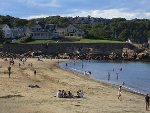 Guests can enjoy a variety of activities on the sandy beach, surrounded by traditional houses on a hillside with lush greenery.