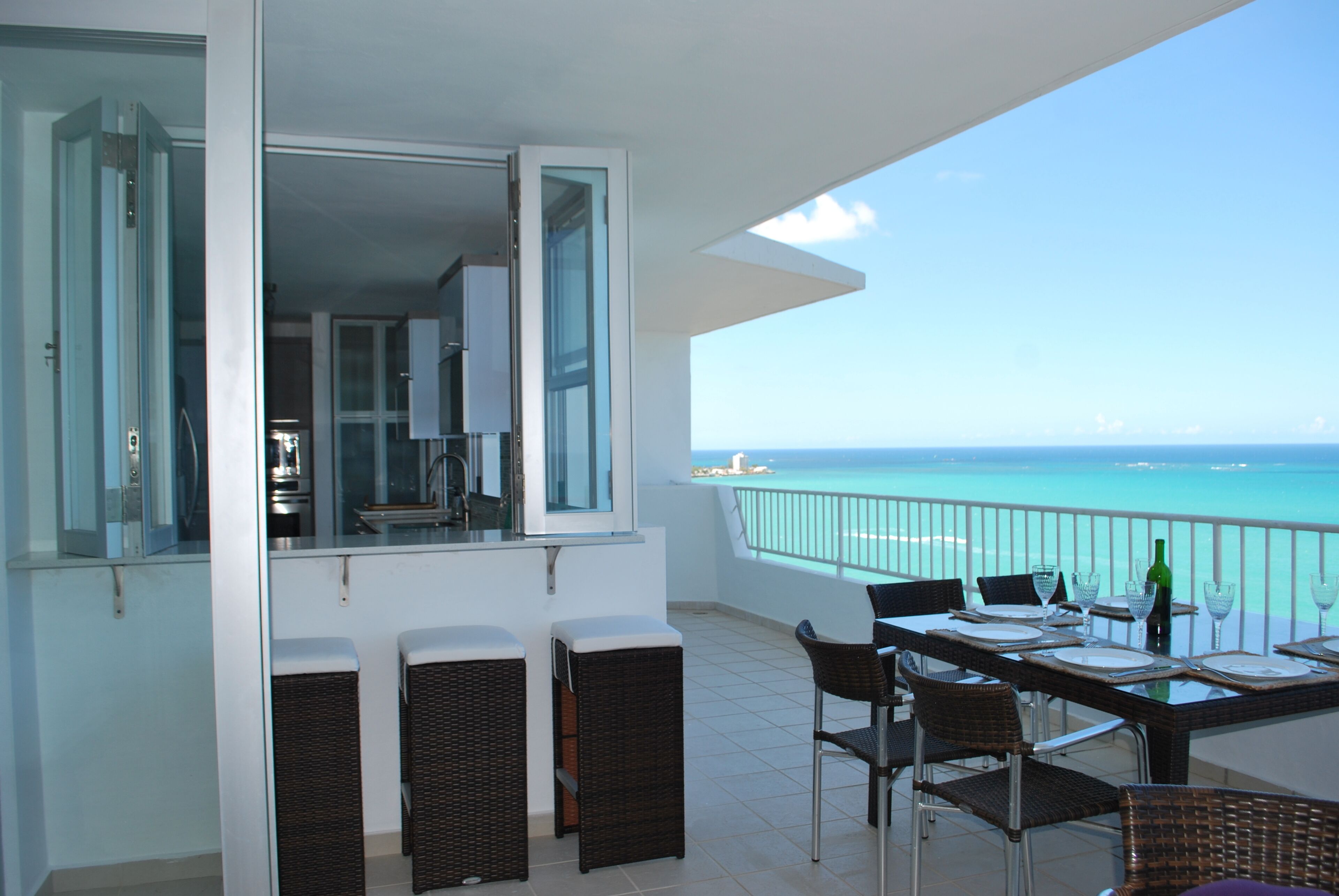 A balcony with a dining table set for two, overlooking a turquoise sea.