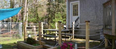 A rustic wooden house with a brick exterior, a wooden deck with benches, and a fenced garden area.
