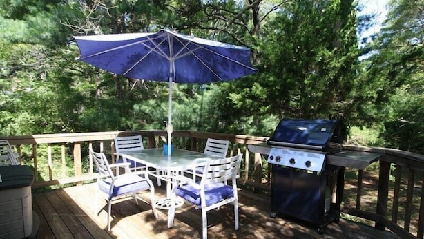 Une terrasse en bois avec une table et des chaises, un barbecue et un parasol.