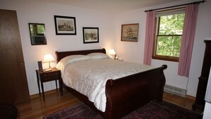 Une chambre à coucher avec un lit en bois, deux tables de chevet avec des lampes, une grande fenêtre avec des rideaux et trois tableaux encadrés accrochés au mur.