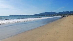 Una playa con cielo despejado, mar tranquilo y montañas al fondo.