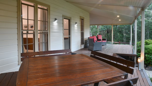 A wooden deck with a table and benches, surrounded by white walls and glass doors. - Fernridge Farm Cottage (Bellingen)