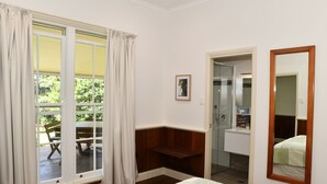 A bedroom with a large window, a wooden bench, a mirror, and a framed picture on the wall. - Fernridge Farm Cottage (Bellingen)