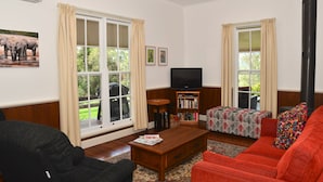 A living room with a sofa, a coffee table, a bookshelf, and a fireplace. - Fernridge Farm Cottage (Bellingen)