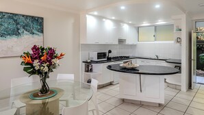 Una cocina moderna con armarios blancos, una isla central y un comedor con mesa y sillas de vidrio.