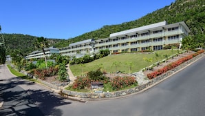 Un hotel de varios pisos con un jardín ajardinado y una carretera delante.