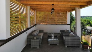 A covered outdoor seating area with wicker furniture, wooden slats, and a view of greenery.