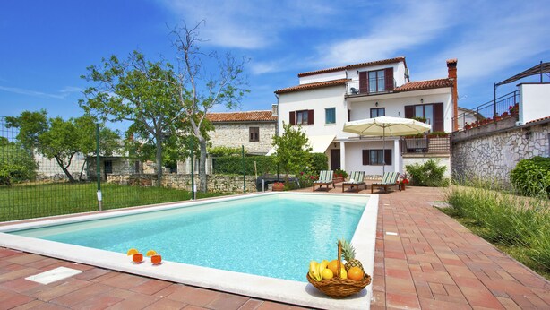 A swimming pool with a stone wall and a white building in the background.