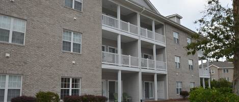 A multi-story brick building with a central balcony and a covered entrance.