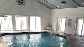 En indendørs swimmingpool med klart vand, et skilt der angiver 3 fod dybde, og en stol ved poolen.