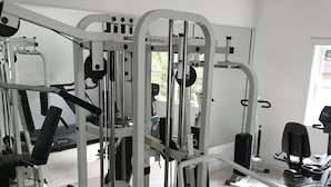 Et fitnessrum med diverse træningsmaskiner, en bænk og et spejl.