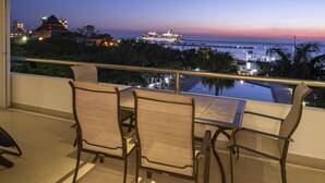 A balcony with a table and chairs, overlooking a body of water with a cruise ship and buildings in the background. - 5 Star Luxury Condo with Awesome Ocean View!  (Cozumel)