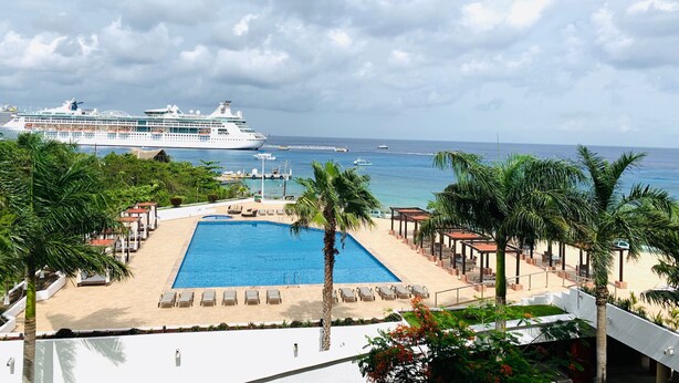 A pool area with lounge chairs, palm trees, and a view of a cruise ship in the distance. - 5 Star Luxury Condo with Awesome Ocean View!  (Cozumel)