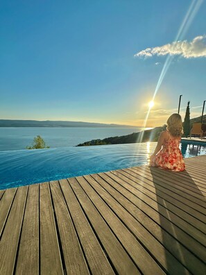 A wooden deck with a pool overlooking a body of water and a sunset. - Luxury villa • Breathtaking views • Prime location (Mimice)