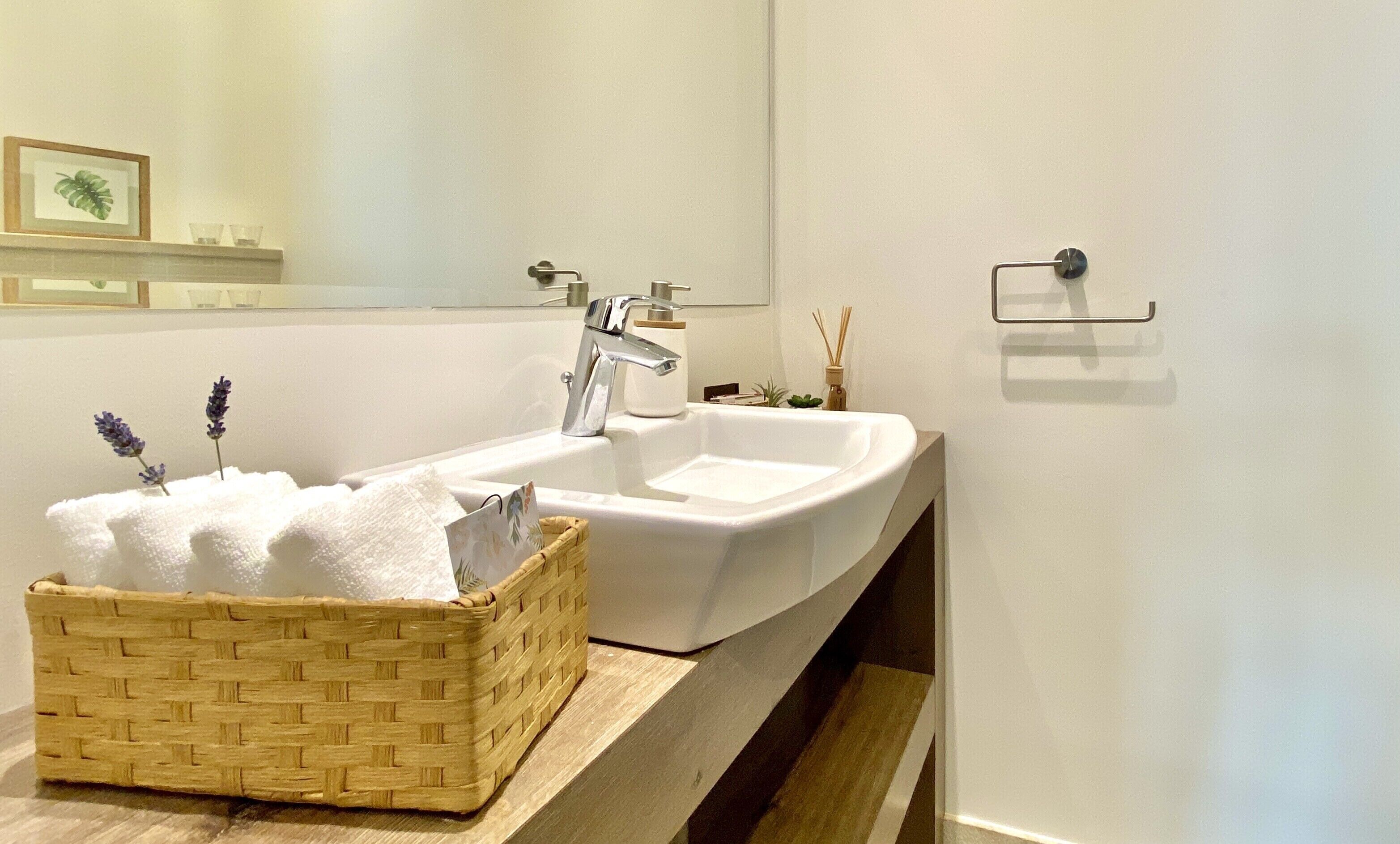 A modern bathroom with a white sink, a wooden basket, and a mirror on the wall.