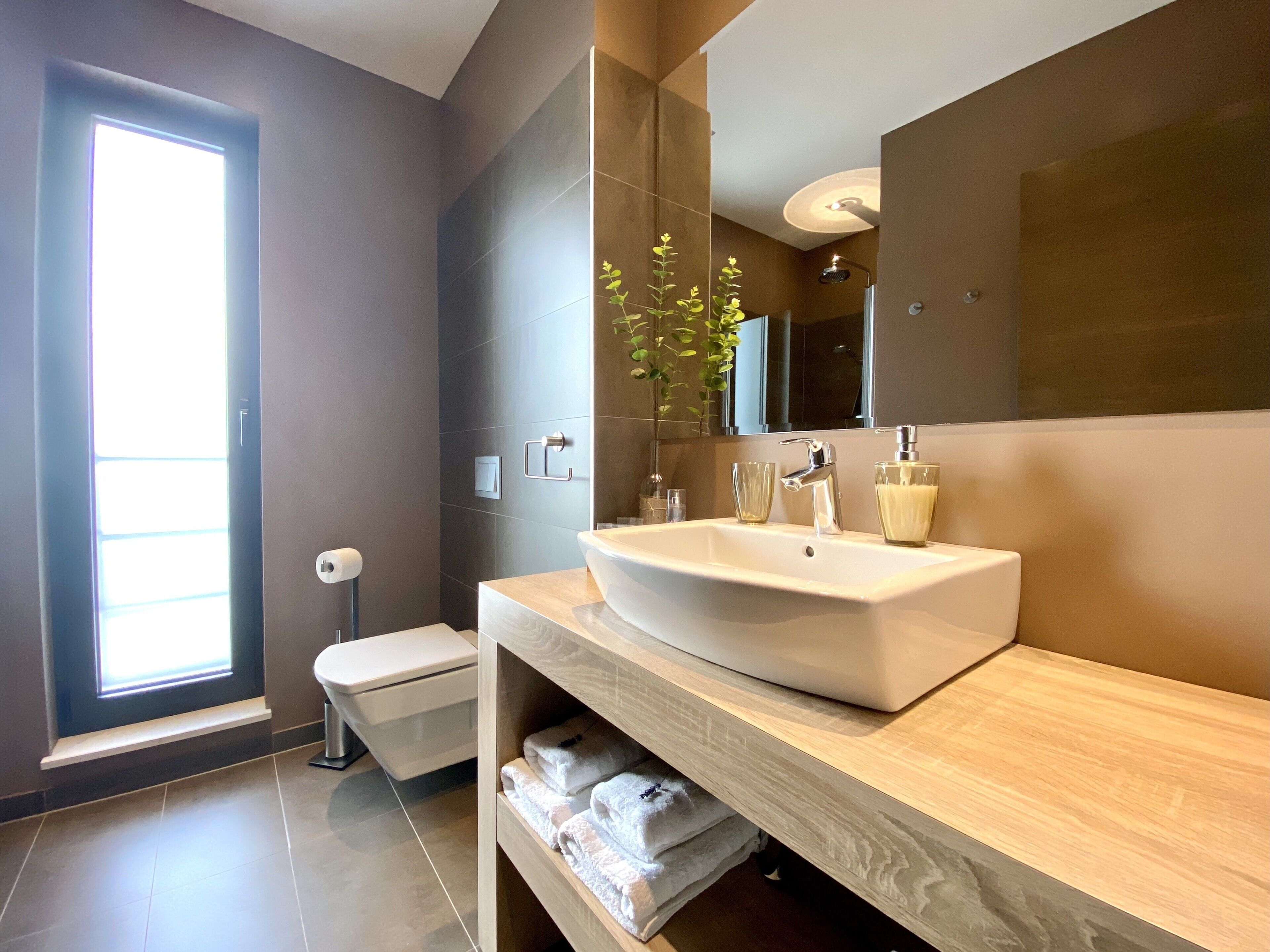 A modern bathroom with a large sink, mirror, and toilet.
