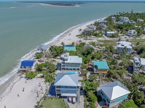 An aerial view of a coastal residential area with houses, a beach, and a large body of water.