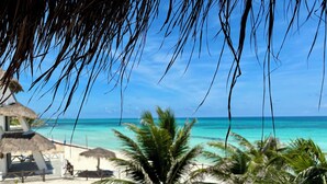 Una playa con palmeras, una estructura de techo de paja y un cielo azul despejado.