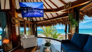 Una habitación con televisión, piso de madera, sofá, mesa de centro y vista al océano.