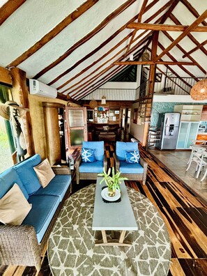 Un intérieur chaleureux avec un plafond haut, un ensemble de canapés, une table basse et un coin cuisine.