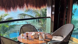 Una mesa redonda de madera con sillas de mimbre en un balcón con vista a una piscina y palmeras.