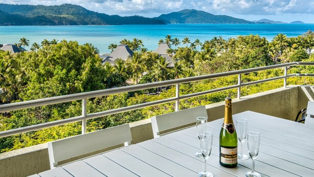Ein Balkon mit Tisch für zwei Personen, mit Blick auf das türkisblaue Meer und üppiges Grün.