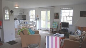 Een woonkamer met een bank, stoelen, een televisie en een eethoek met een tafel en stoelen.