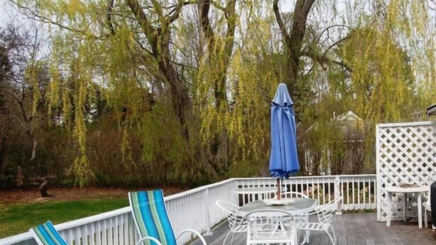 Een houten terras met witte relingen, blauw-gestreepte ligstoelen en een tafel met stoelen.