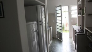 Une cuisine équipée d’appareils électroménagers en acier inoxydable, dotée d’un sol carrelé et offrant une vue sur un jardin grâce à une porte ouverte.