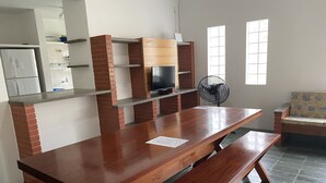 Une cuisine spacieuse avec une longue table en bois et des bancs, un mur décoratif en briques, un four encastré et un ventilateur.