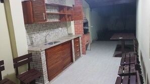 Une cuisine compacte avec un dosseret carrelé, un four encastré et des placards en bois. L’espace repas comprend un banc et une table avec des chaises.