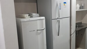 Une cuisine de taille réduite, avec un réfrigérateur blanc et un petit appareil électroménager, peut-être une machine à café, posé sur le plan de travail.