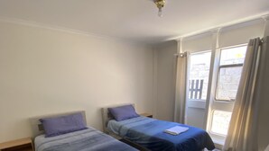 A room with two beds, wooden flooring, a window with curtains, and a ceiling light fixture. - Murchison Waters Accommodation (Kalbarri)