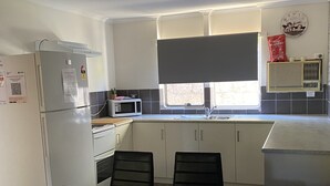 A compact kitchen with a refrigerator, microwave, sink, and a dining area with chairs. - Murchison Waters Accommodation (Kalbarri)
