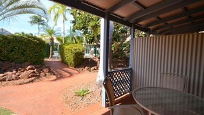 Un espace extérieur abrité, doté d’une table et de chaises, entouré d’un jardin avec des palmiers et d’un chemin en briques.