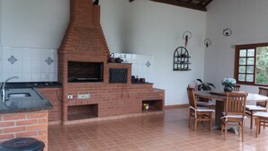 A kitchen with a brick oven, a sink, and a dining area with chairs and a table. - Excellent Country House (Água Preta)