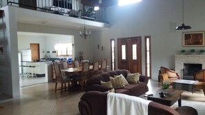 A spacious living room with a brown sofa, a dining area with wooden chairs, a kitchen in the background, and a fireplace. - Excellent Country House (Água Preta)